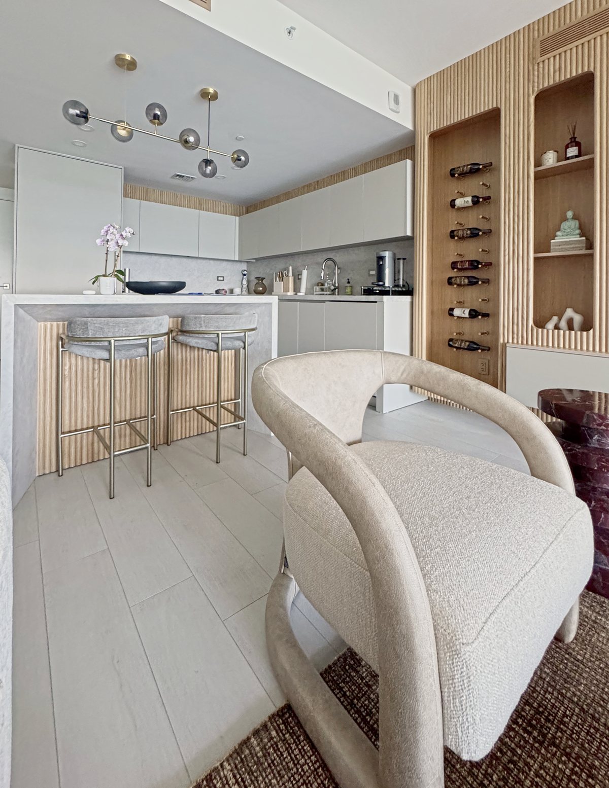 Kitchen bar with stools under a globe chandelier and a bouclé armchair