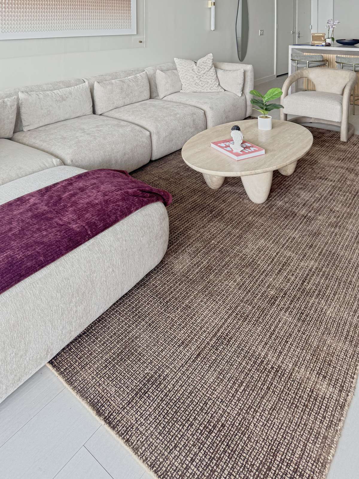 A pale sectional with a plum throw, a sculptural coffee table and a textured rug
