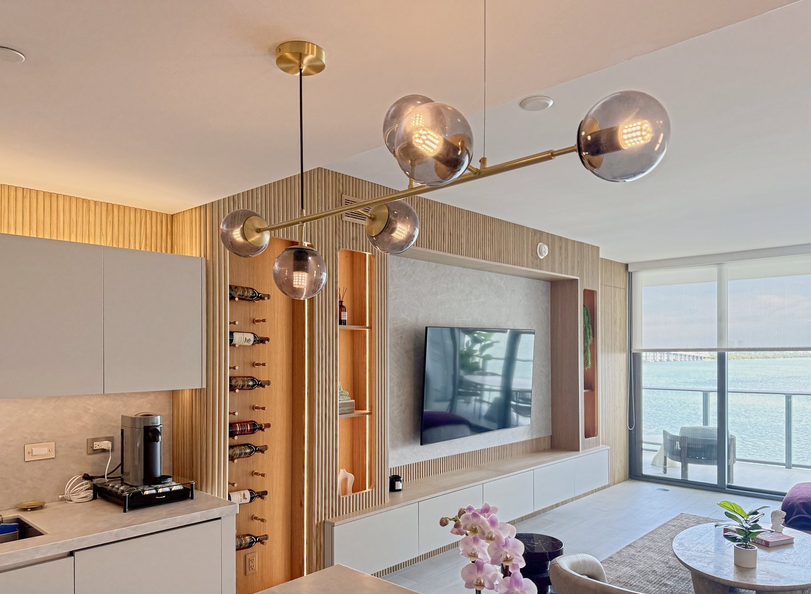 Media wall in fluted oak with lit niches and a wine wall under a brass and smoked-glass pendant